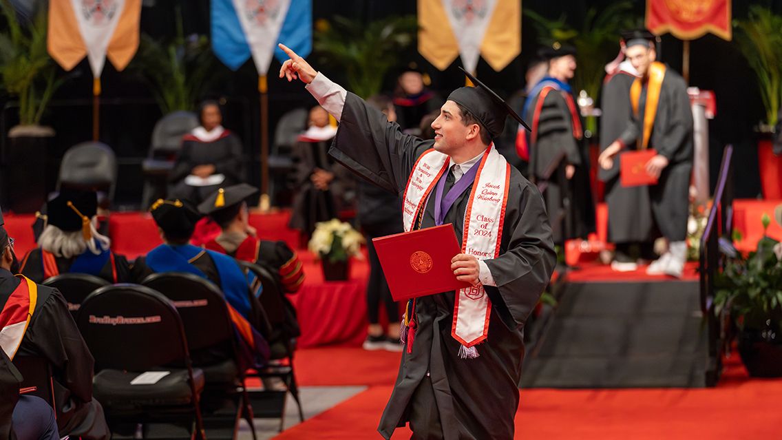A Bradley graduate points to the crowd and smiles after he crosses the stage during December Commencement.