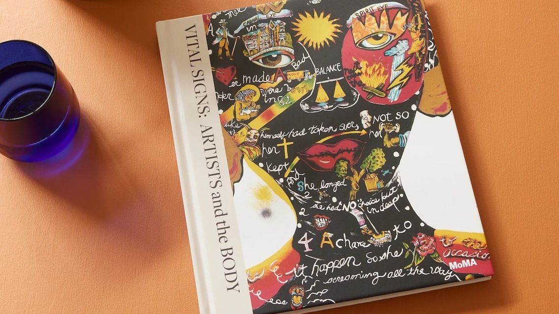 A hardcover book, Vital Signs: Artists and the Body, rests on a table by a glass of water