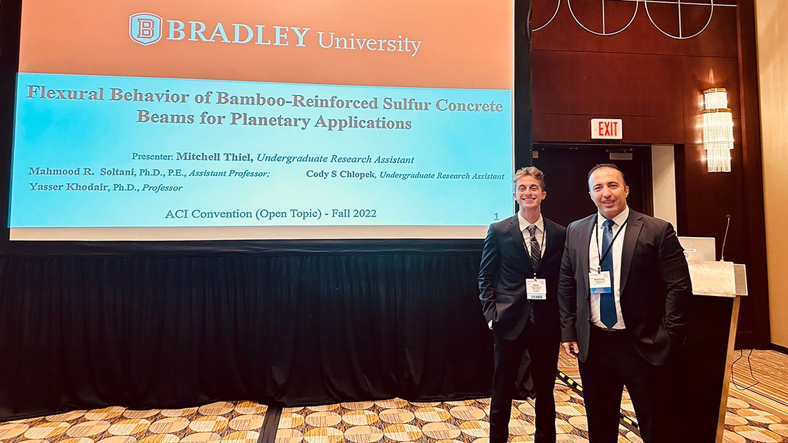 Professor and Student stand next to presentation screen